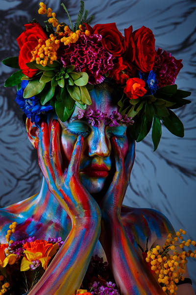 Portrait of a girl whose face is painted with colored paints in a wreath of flowers. In Frida Kahlo's footsteps