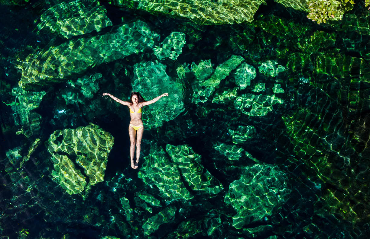 Overhead shot of a attractive young brunette woman in a bikini floating in the Cristalino cenote near Tulum, Mexico