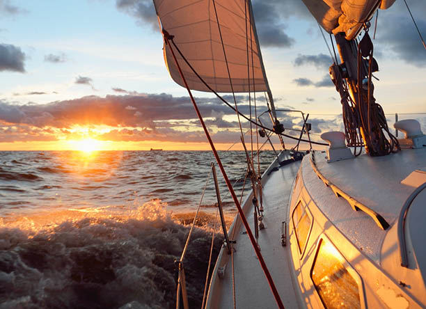 Yacht sailing in an open sea at sunset. Close-up view of the deck, mast and sails. Clear sky after the rain, dramatic glowing clouds, golden sunlight, waves and water splashes, cyclone. Epic seascape