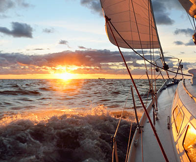Yacht sailing in an open sea at sunset. Close-up view of the deck, mast and sails. Clear sky after the rain, dramatic glowing clouds, golden sunlight, waves and water splashes, cyclone. Epic seascape