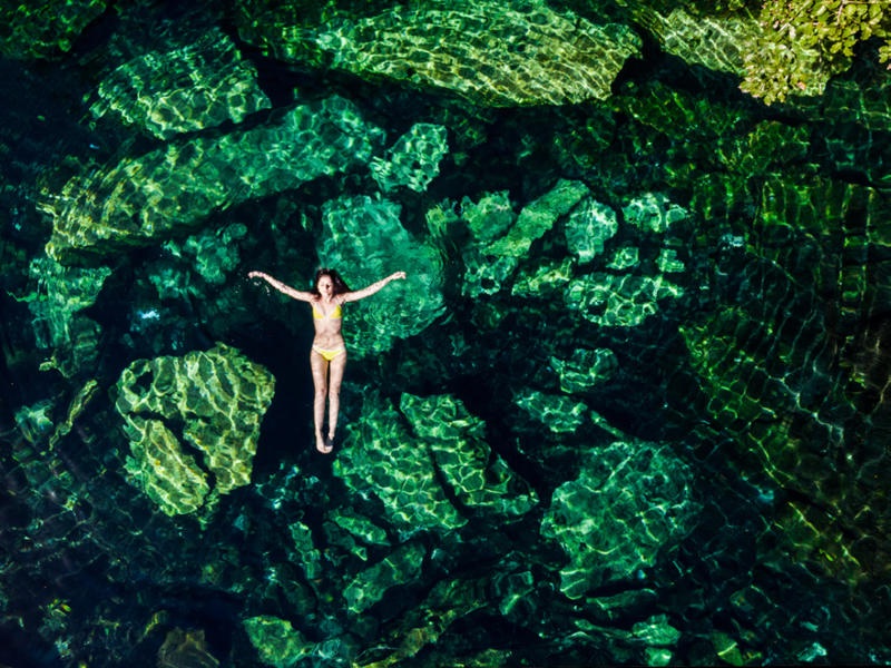 Overhead shot of a attractive young brunette woman in a bikini floating in the Cristalino cenote near Tulum, Mexico