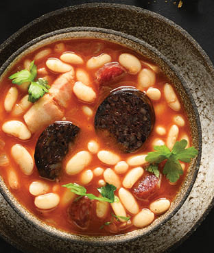 Asturiana spanish fabada with chorizo, morcilla, sausage, haricot served fresh toast on black background with copy space. Top view. Tasty traditional spanish warming dinner.