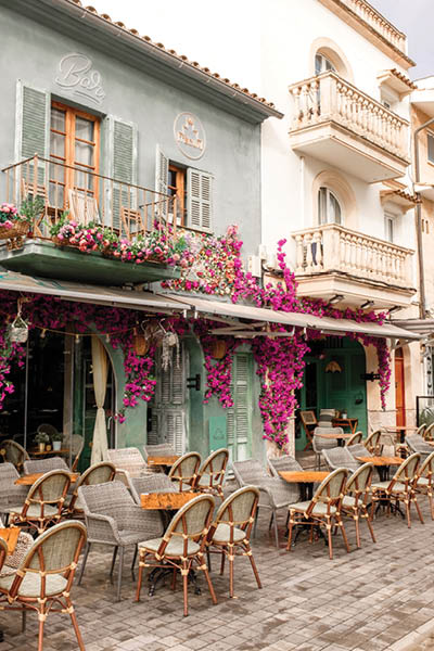 Puerto Pollensa, Mallorca, Spain - October 28 2024: Pretty early morning scene outside the Tecun Bar before opening time showing hanging fuchsia flowers and unoccupied tables and chairs.