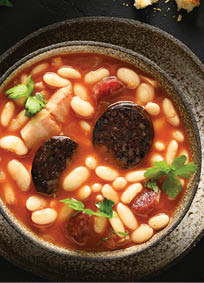 Asturiana spanish fabada with chorizo, morcilla, sausage, haricot served fresh toast on black background with copy space. Top view. Tasty traditional spanish warming dinner.