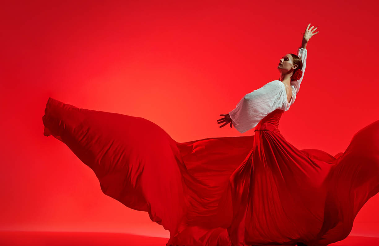 Passionate woman, flamenco dancer in stylish costume with skirt spreads like wings, performing against vivid red background. Concept of art of movement, classical dance, beauty, festival