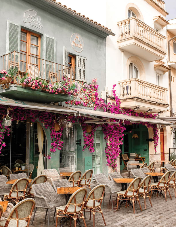 Puerto Pollensa, Mallorca, Spain - October 28 2024: Pretty early morning scene outside the Tecun Bar before opening time showing hanging fuchsia flowers and unoccupied tables and chairs.