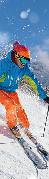 A skier skiing downhill a groomed alpine slope during sunny winter day