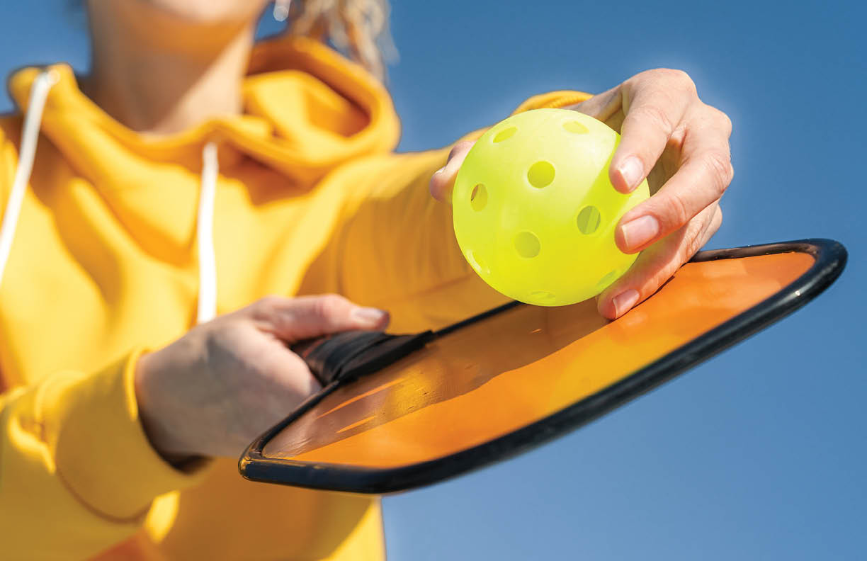 Pickleball paddle and yellow ball close up, woman playing pickleball game, hitting pickleball yellow ball with paddle, outdoor sport leisure activity