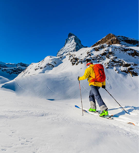 Man backcountry skiing on powder snow with Matterhorn in background, Zermatt in Swiss Alps.