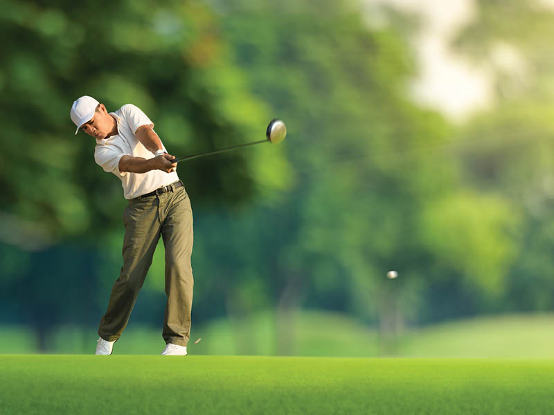 Golfer hitting golf ball with driver.