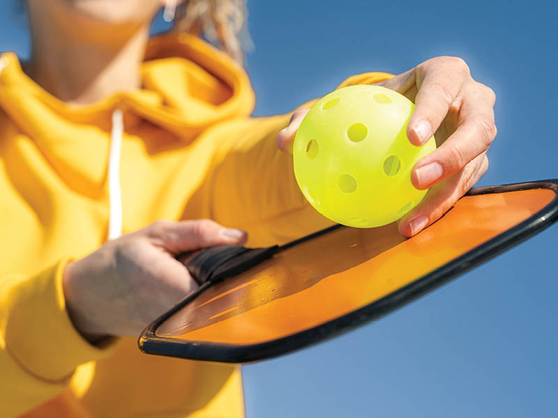 Pickleball paddle and yellow ball close up, woman playing pickleball game, hitting pickleball yellow ball with paddle, outdoor sport leisure activity