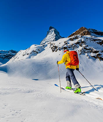Man backcountry skiing on powder snow with Matterhorn in background, Zermatt in Swiss Alps.
