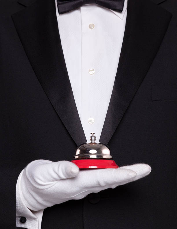 Waiter in black tie and white gloves holding a service bell.