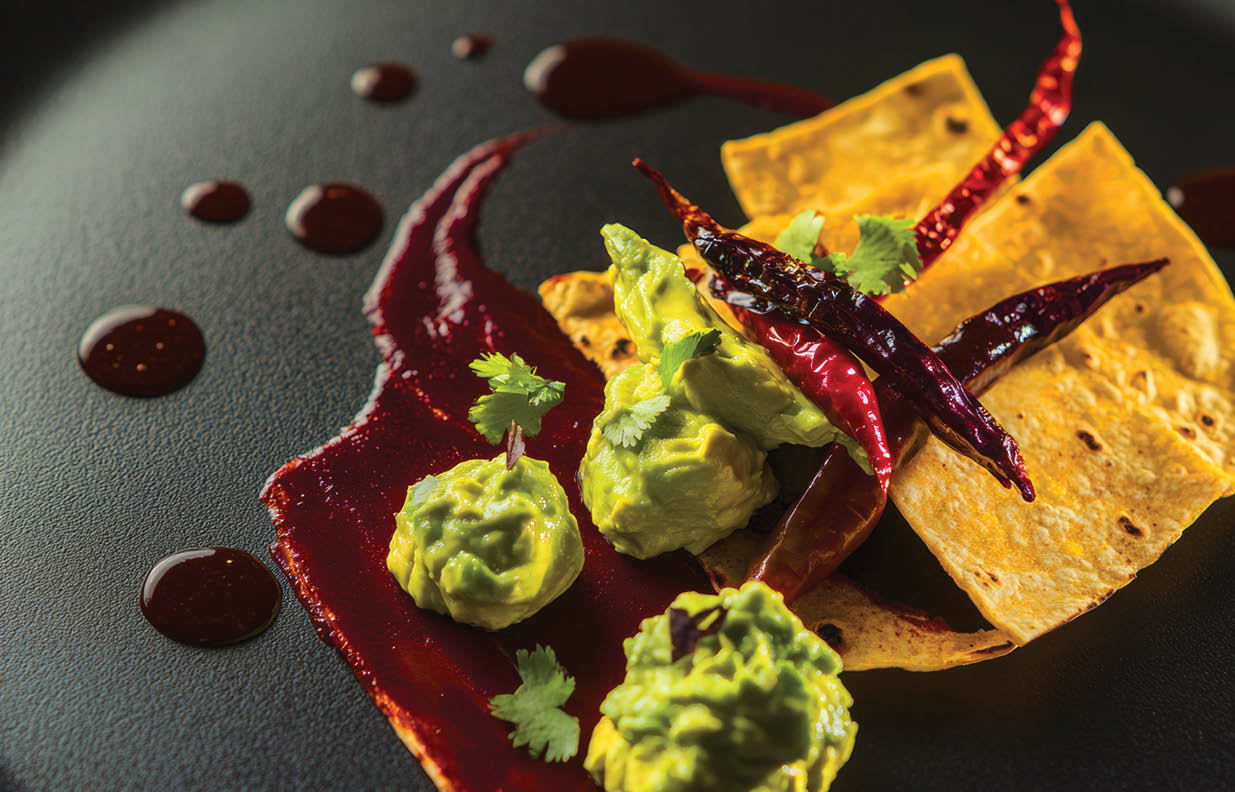 Gourmet mexican appetizer with guacamole and chili peppers on black plate.