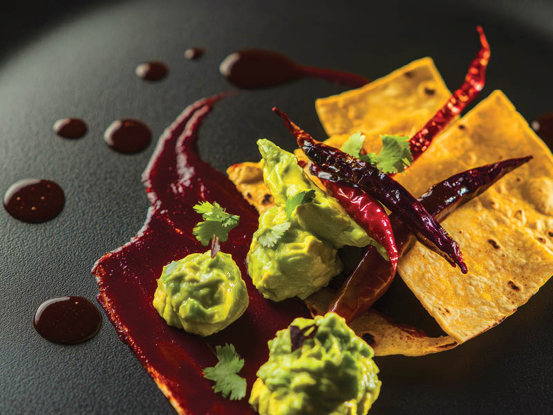 Gourmet mexican appetizer with guacamole and chili peppers on black plate.