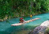 Falmouth, Jamaica - July 07 2019: Martha Brae River, Jamaica. Tourists on bamboo raft rides. Relaxing scenic tour in countryside landscape under canopy trees. People enjoy summer vacation activity.