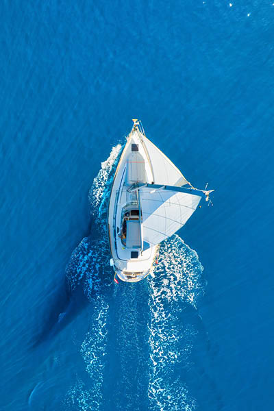 Wave and sail yacht on the sea as a background. Sea and waves from top view. Blue water background from top view. Top view from drone. Summertime vacation. Travel image