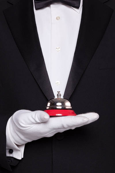 Waiter in black tie and white gloves holding a service bell.