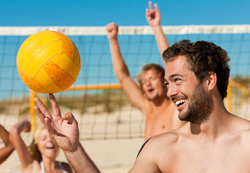Group of friends - women and men - playing beach volleyball, one in front doing tricks to the ball