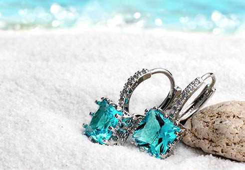Jewelry earrings with aquamarine on sand beach background, soft focus
