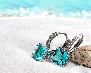 Jewelry earrings with aquamarine on sand beach background, soft focus
