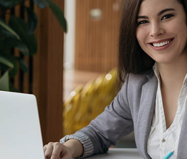 Portrait of beautiful confident businesswoman using laptop computer taking notes working online in office. Smiling student studying looking at camera sitting modern library, education concept