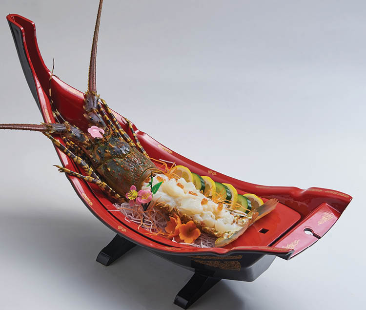 Fresh lobster sashimi served on a boat shaped plate, decorated with delicious seafood dishes.