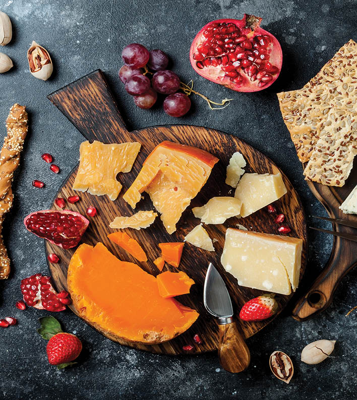 Cheese variety board or platter with cheese assortment, grapes, honey, nuts. Black stone background. Top view, flat lay