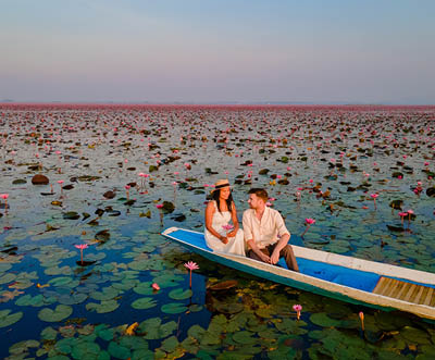 The sea of red lotus, Lake Nong Harn, Udon Thani, Thailand, a couple of men and woman in a boat at sunrise at the Red Lotus Lake in the Isaan at sunrise