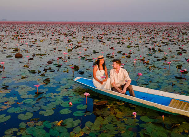The sea of red lotus, Lake Nong Harn, Udon Thani, Thailand, a couple of men and woman in a boat at sunrise at the Red Lotus Lake in the Isaan at sunrise