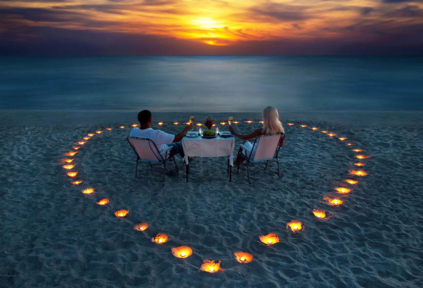 A young couple share a romantic dinner with candles heart on the sea sand beach