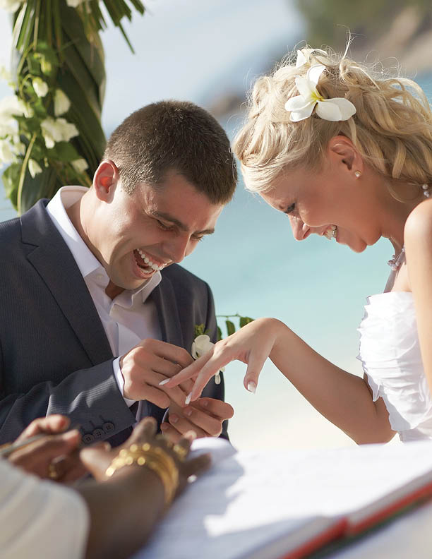 Just married newlyweds couple exchange rings, groom puts the ring on the bride's hand during beautiful tropical ceremony.