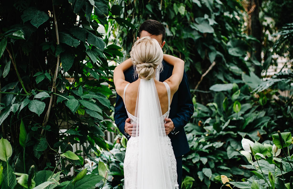 Portrait the groom and the bride standing back and kissing on the background of greenery. Wedding ceremony in Botanical green garden.