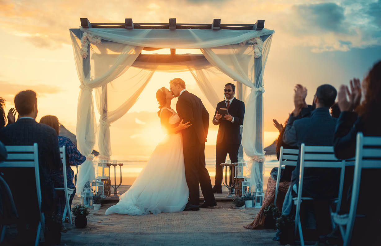 Beautiful Bride and Groom During an Outdoors Wedding Ceremony on an Ocean Beach at Sunset. Perfect Venue for Romantic Couple to Get Married, Exchange Rings, Kiss and Share Celebrations with Friends.