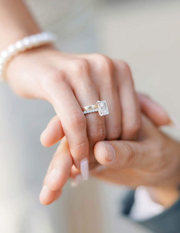 The groom gently holds the hand of the bride with a wedding ring. Hands of the bride and groom close-up. A wedding ring with a large gemstone is worn on the bride's hand