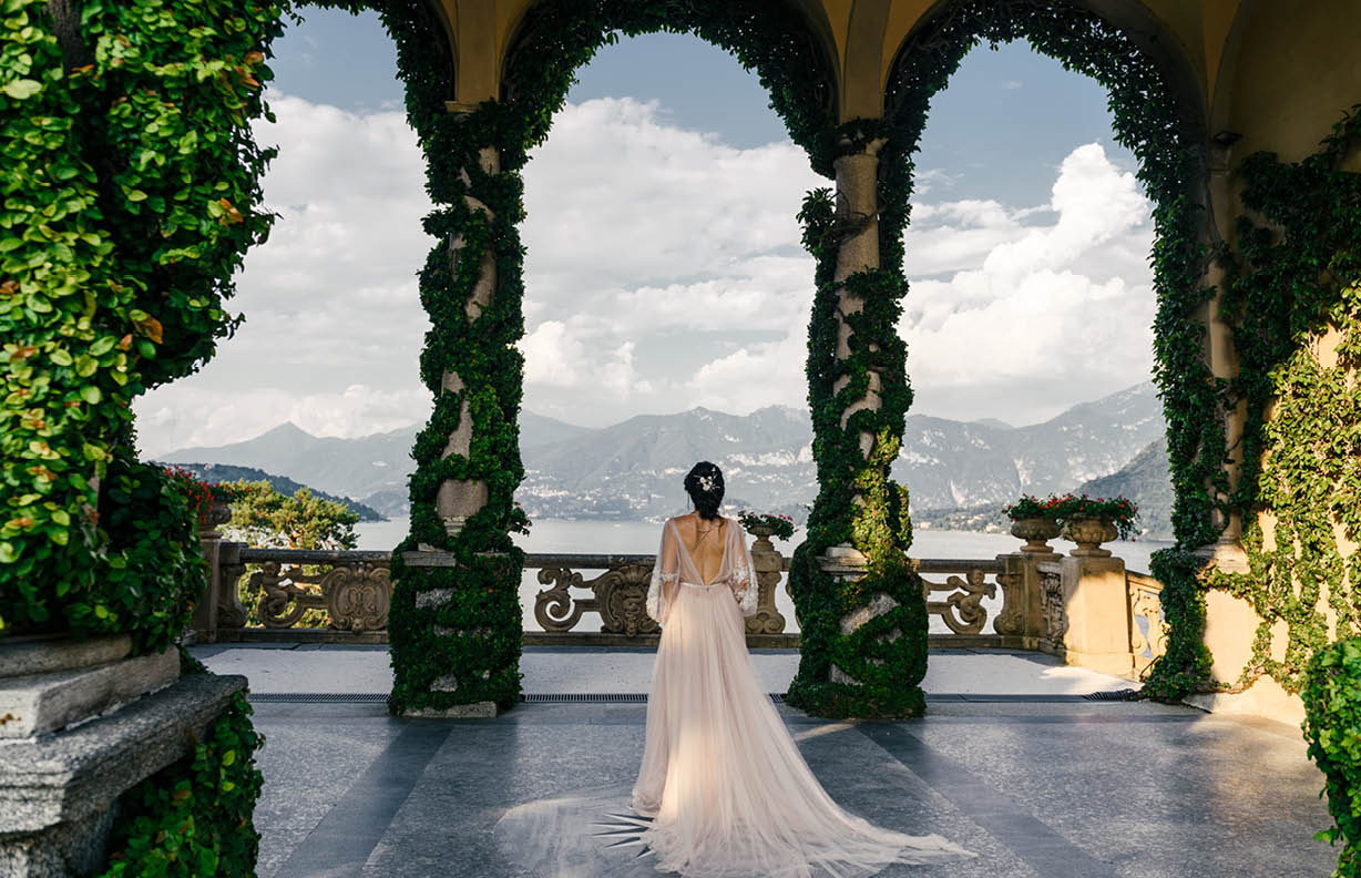 Bride in a wedding dress stands on a beautiful balcony overlooking mountains and lake