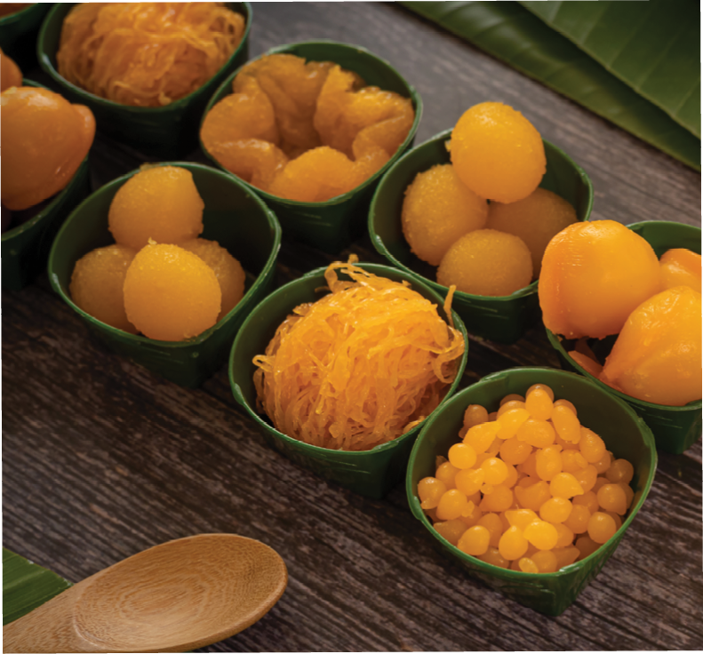 a variety of elegantly beautiful Thai Desserts (Khanom Wan Thai) serving in a wooden plate on a dark wooden table. The bites in gold color and different flower shapes.Thai dessert, Auspicious dessert