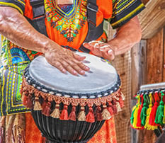 Man in colorful costume plays African ethnic percussion drum with tassels against blurred background - cropped and motion blur on hands
