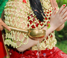 A traditional Indonesian siraman ritual, where water is poured over a bride-to-be, symbolizing purification and blessings before the wedding, performed with floral attire and a brass ladle.