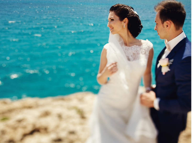 Elegant smiling young bride and groom walking on the beach, kissing and having fun, wedding ceremony near the rocks and ocean