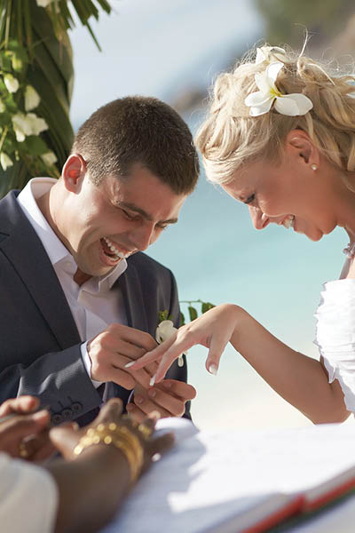 Just married newlyweds couple exchange rings, groom puts the ring on the bride's hand during beautiful tropical ceremony.