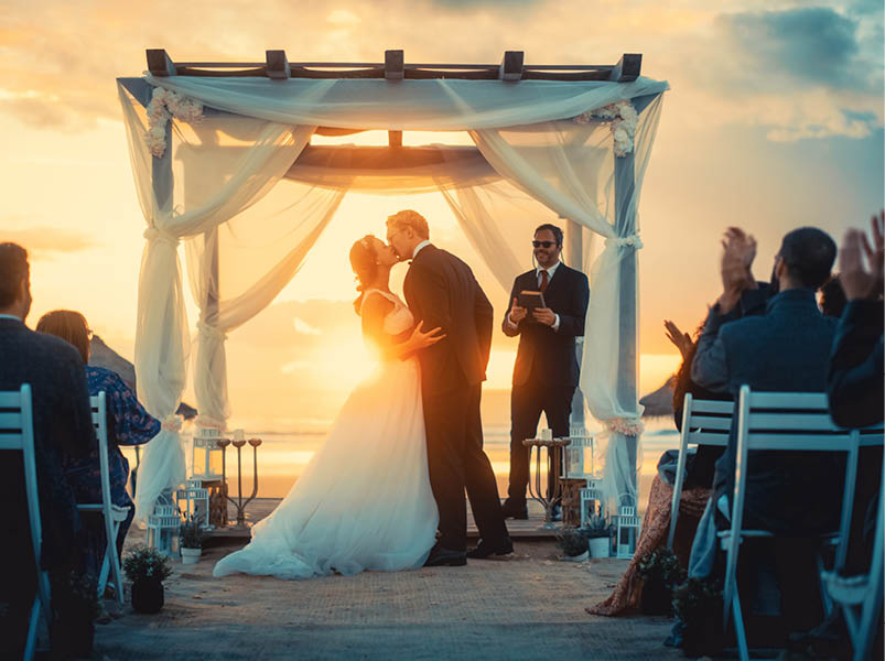 Beautiful Bride and Groom During an Outdoors Wedding Ceremony on an Ocean Beach at Sunset. Perfect Venue for Romantic Couple to Get Married, Exchange Rings, Kiss and Share Celebrations with Friends.