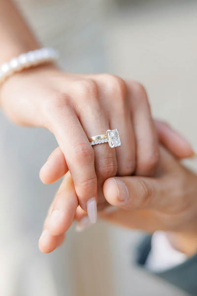 The groom gently holds the hand of the bride with a wedding ring. Hands of the bride and groom close-up. A wedding ring with a large gemstone is worn on the bride's hand