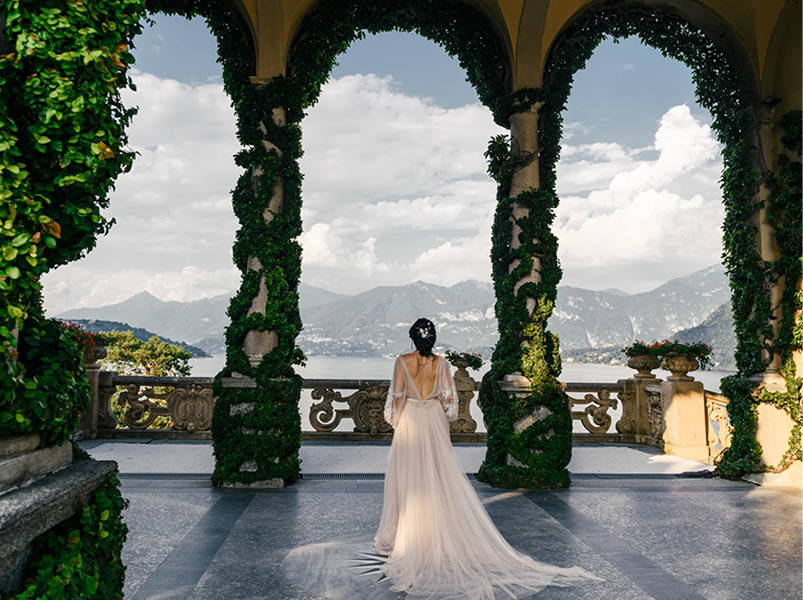Bride in a wedding dress stands on a beautiful balcony overlooking mountains and lake
