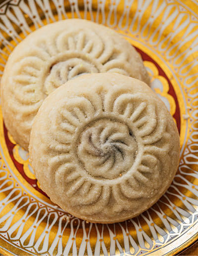 close up of maamoul (ma'amoul), date-filled butter cookies on ornate patterned gold and white plate