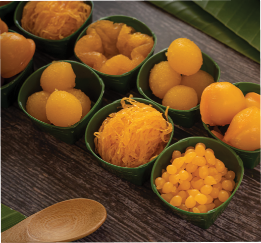 a variety of elegantly beautiful Thai Desserts (Khanom Wan Thai) serving in a wooden plate on a dark wooden table. The bites in gold color and different flower shapes.Thai dessert, Auspicious dessert