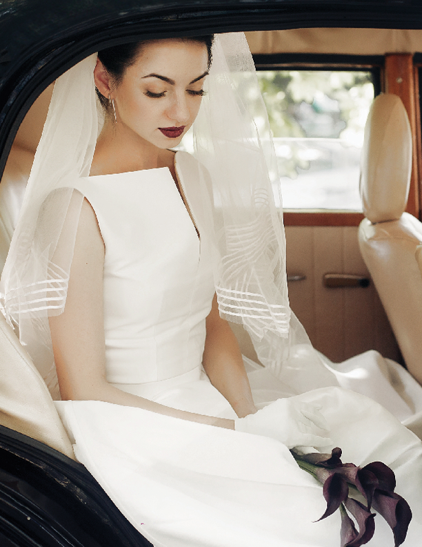 gorgeous elegant bride posing in stylish retro black car, sitting inside in saloon holding bouquet of callas. luxury wedding in vintage style. unusual gown and veil